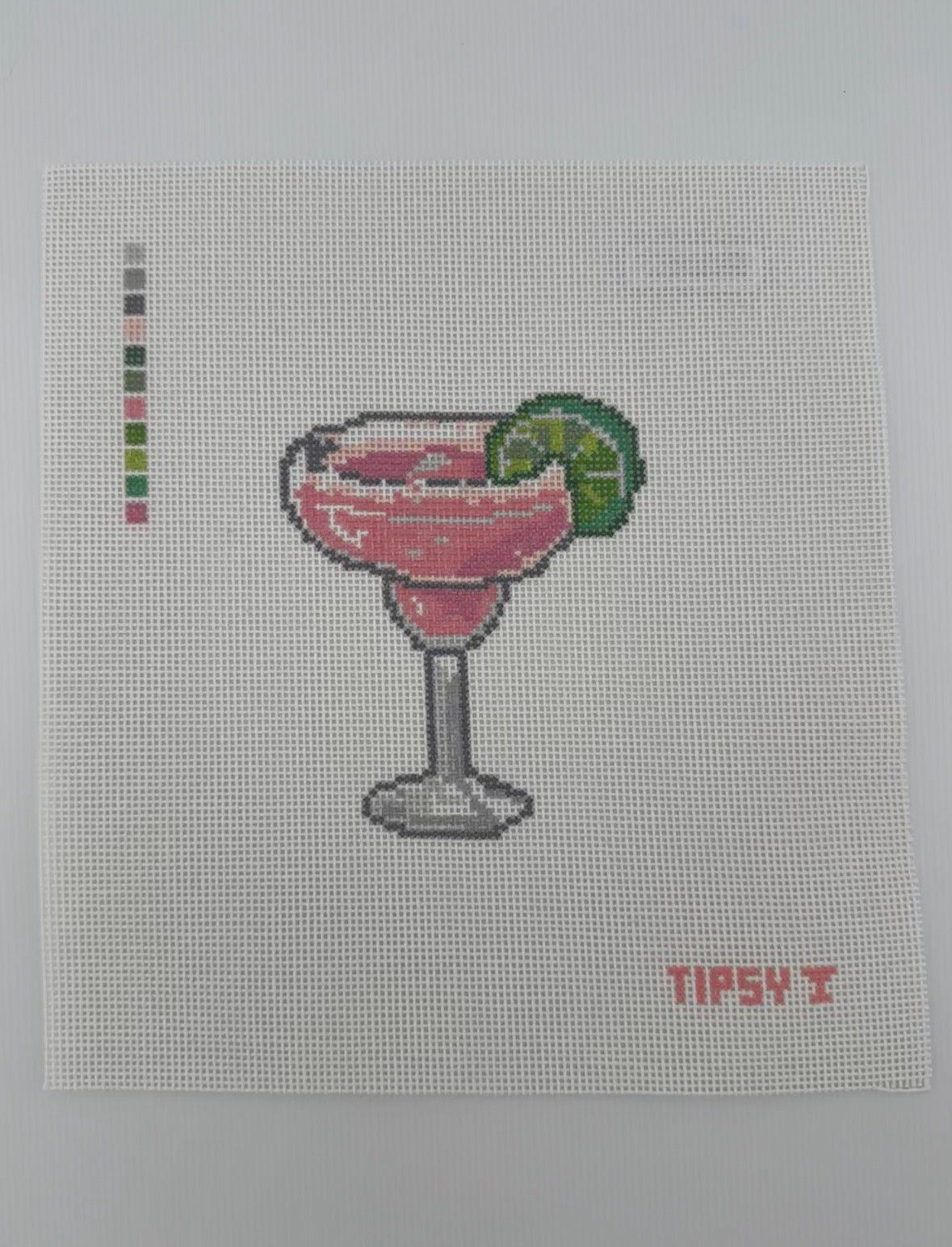 A square 18 mesh needlepoint canvas featuring a pink margarita cocktail in a glass with a lime wedge, on a white background with a small red TIPSY  text at the bottom right.