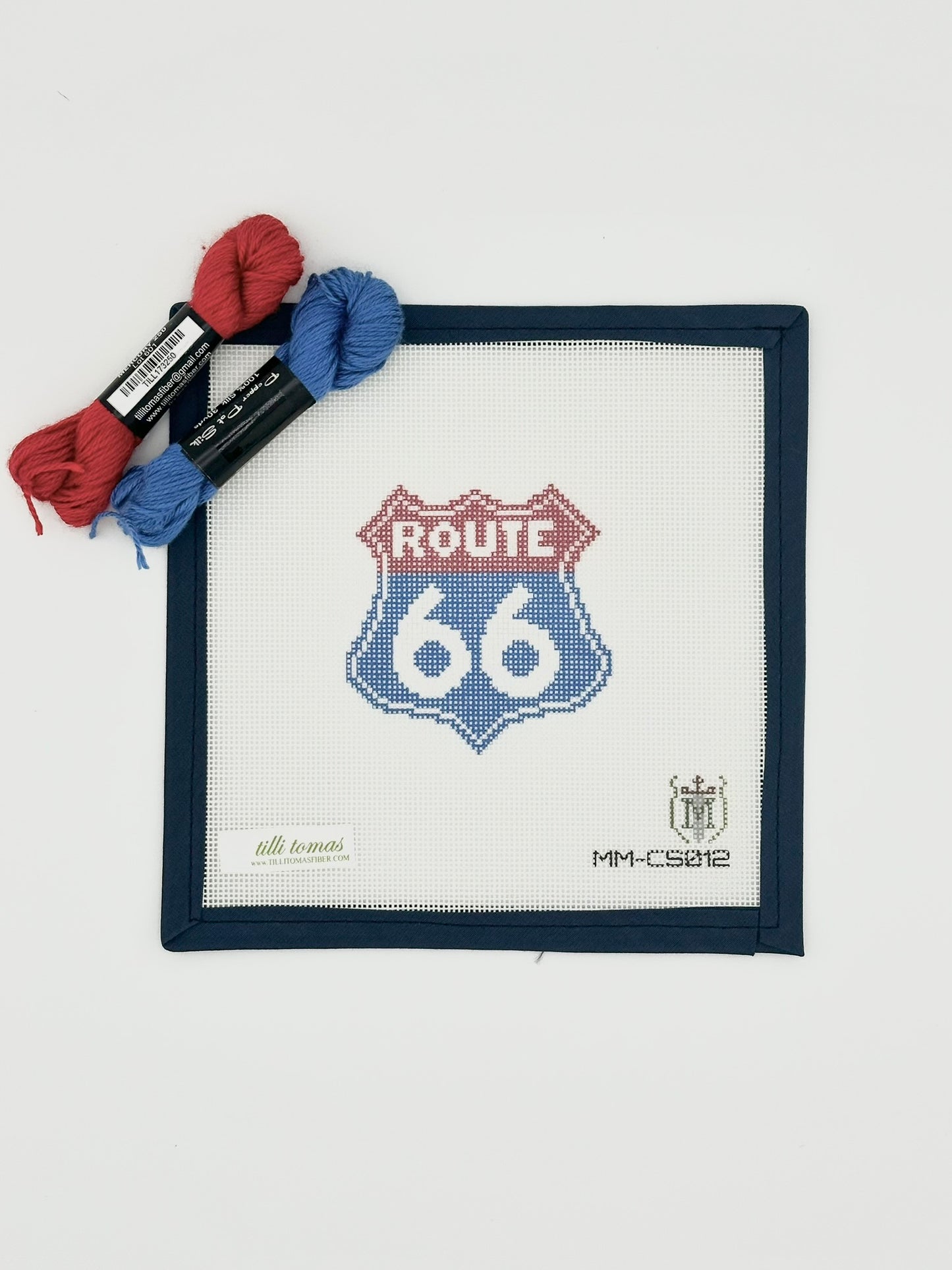 Route 66 needlepoint canvas with blue bias tape shown laying flat on white background with red and blue pepper pot threads laying across the top.
