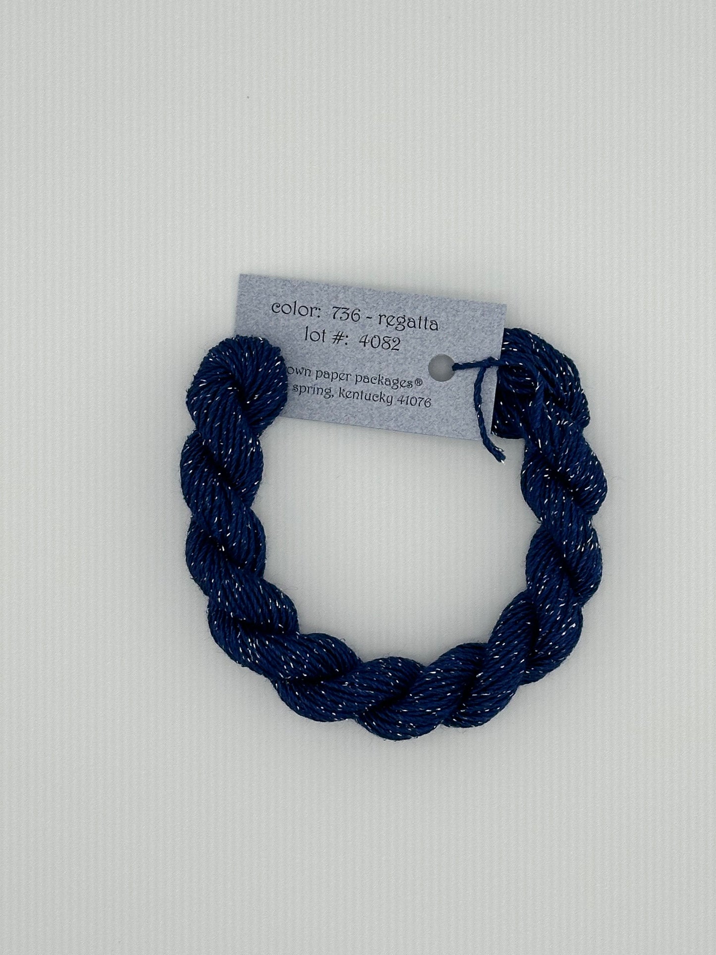 30 yard skein of Stardust Silk and Ivory needlepoint thread in Regatta 735 blue, with light blue label lying flat on white background