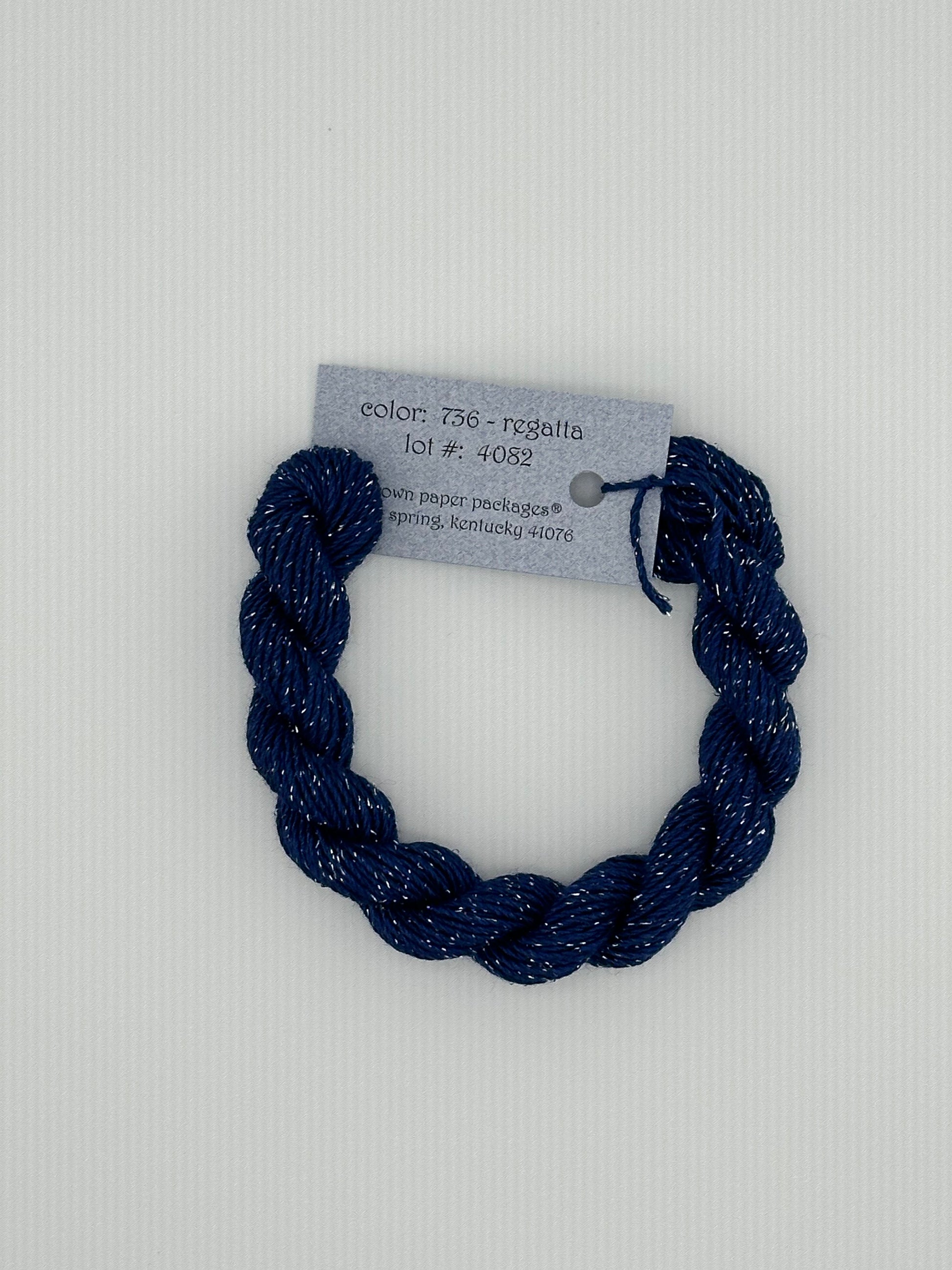 30 yard skein of Stardust Silk and Ivory needlepoint thread in Regatta 735 blue, with light blue label lying flat on white background