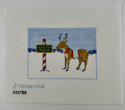 18 mesh needlepoint canvas featuring a Christmas scene with a brown reindeer wearing a red harness, standing next to a red-and-white striped pole with a green sign that reads 'NORTH POLE'. With the brand name 'STITCHSTYLE' and number 'S51700' printed in blue at the bottom left.