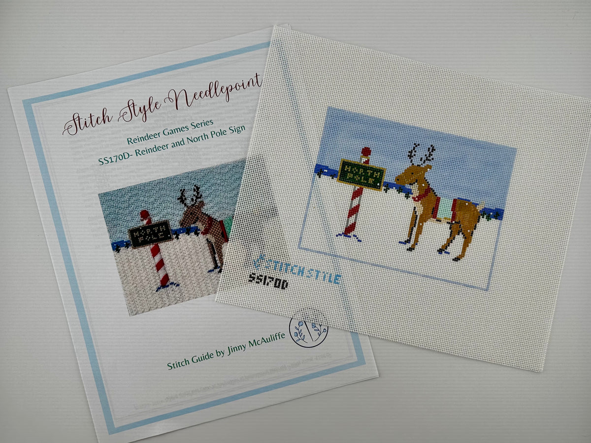 18 mesh needlepoint canvas featuring a Christmas scene with a brown reindeer wearing a red harness, standing next to a red-and-white striped pole with a green sign that reads 'NORTH POLE'. With the brand name 'STITCHSTYLE' and number 'S51700' printed in blue at the bottom left. Shown with stitch guide.
