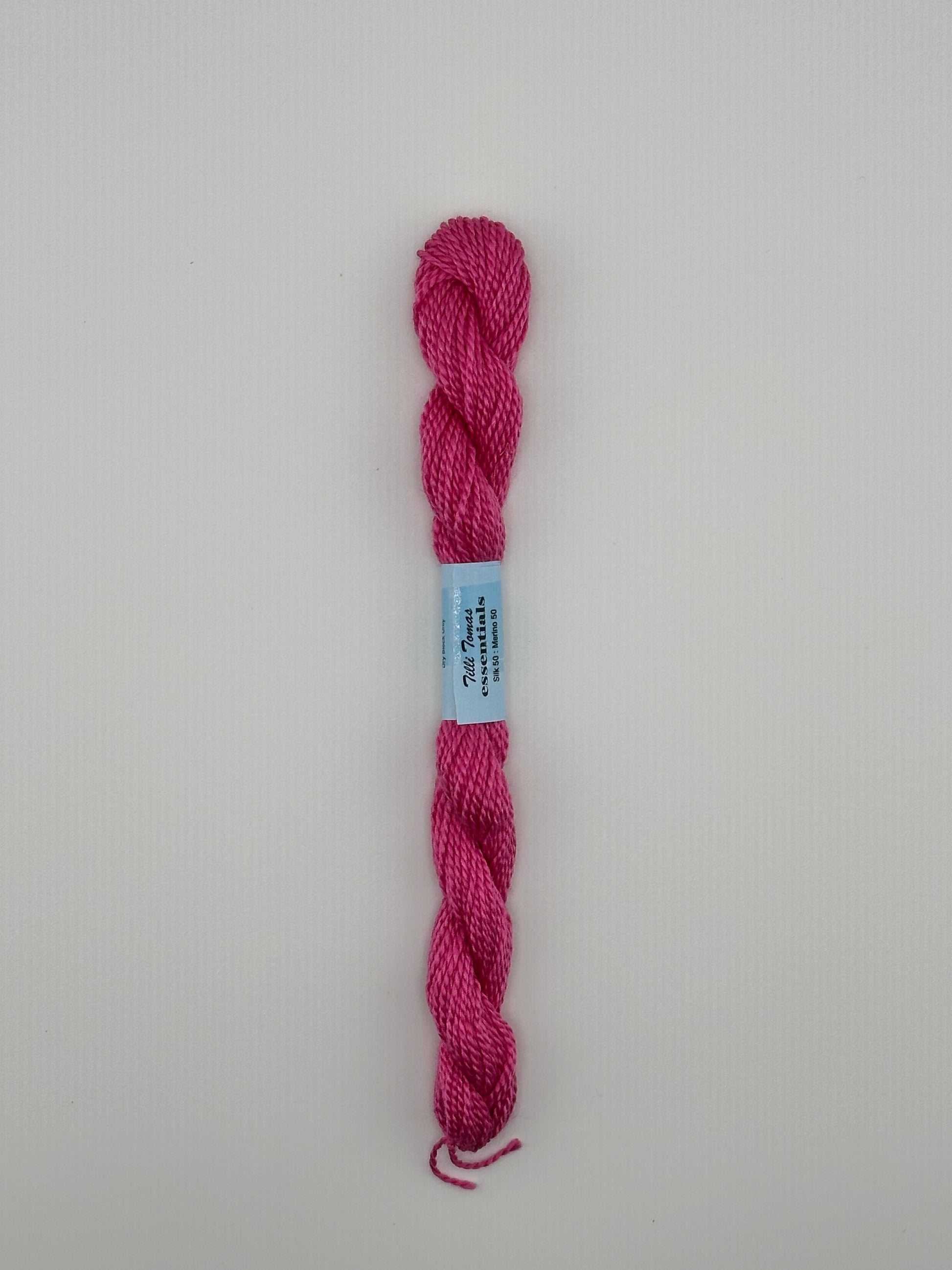 30 yard skein of essentials needlepoint thread in Ribbon S844 pink, with blue label lying flat on white background.