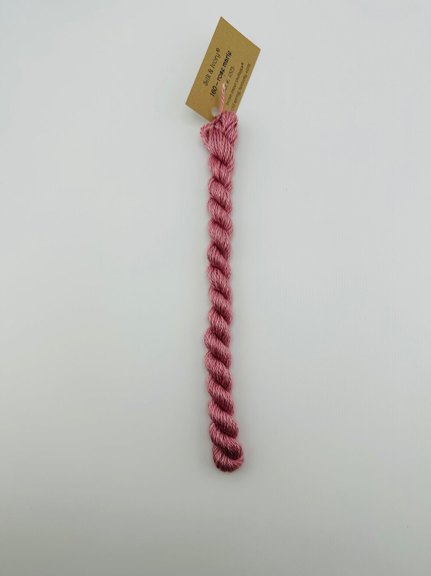 30 yard skein of silk & Ivory in the color 160 Rose Marie with brown tag laying flat on white background
