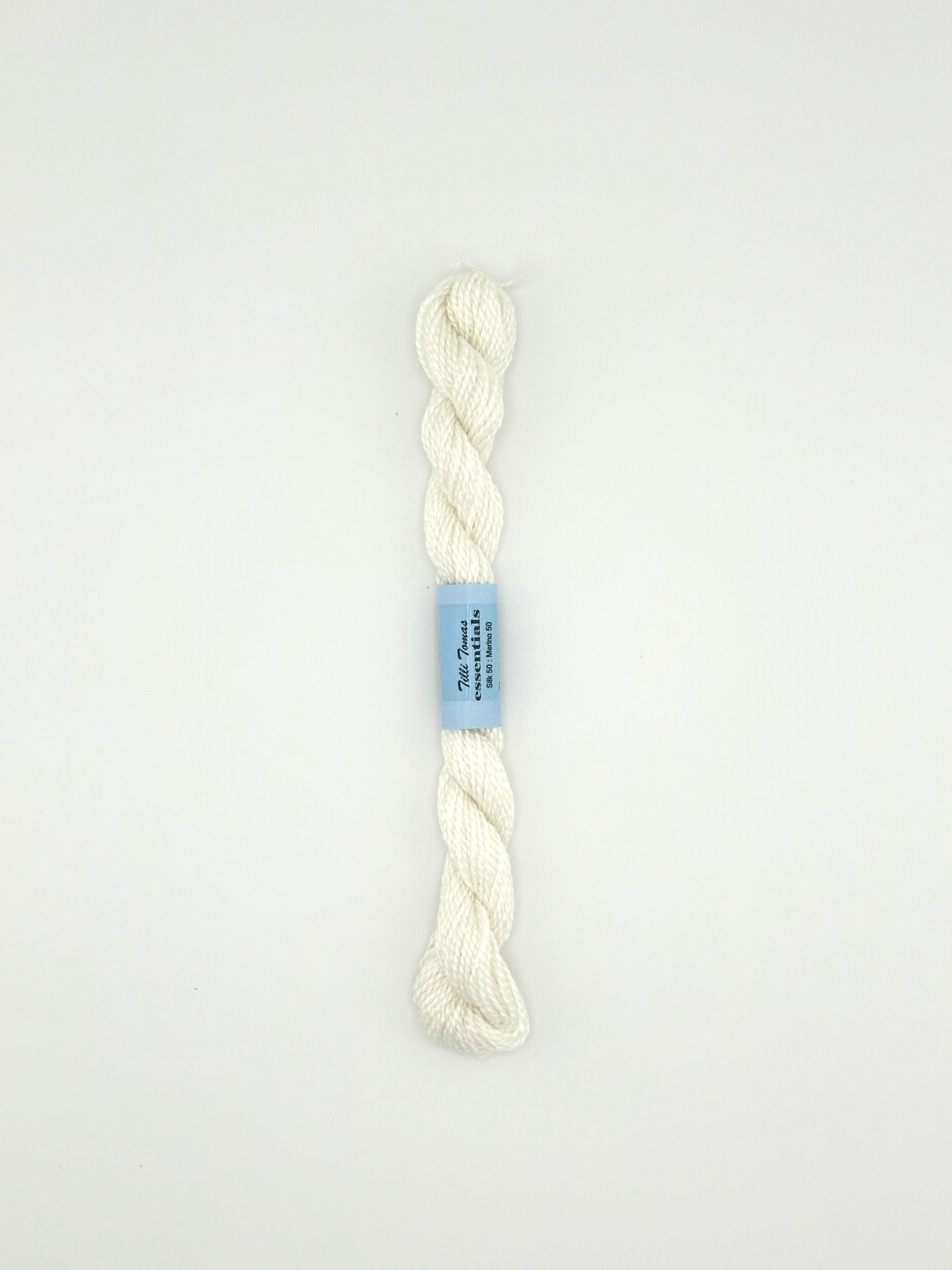 30 yard skein of essentials needlepoint thread in white 502, with blue label lying flat on white background