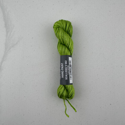 30 yard skein of Pepper Pot Silk needlepoint thread in a green variegated scalllion v082, with black and white label lying flat on white background