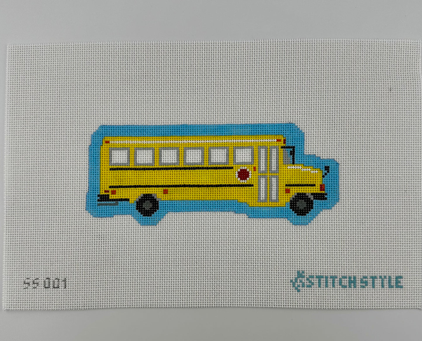 A 18 mesh needlepoint canvas featuring a yellow school bus with black wheels and a blue shadow, on a white background with the Stitchstyle logo in the bottom right corner.