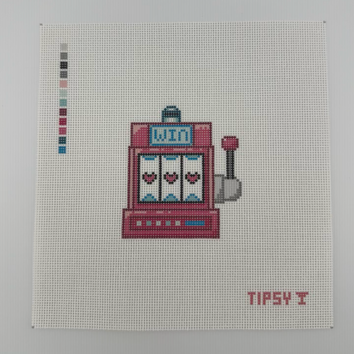 18 mesh needlepoint canvas with pink slot machine with three hearts on the reels, a small blue sign reading 'WIN', and a lever on the right. The canvas is photographed against a white background, with a small color swatch strip on the left and the text TIPSY in the lower right corner.