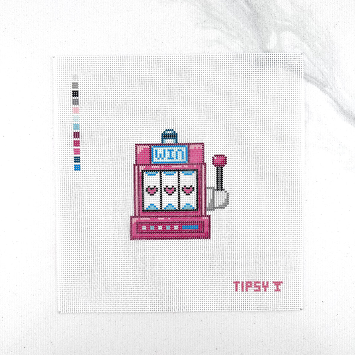 18 mesh needlepoint canvas with pink slot machine with three hearts on the reels, a small blue sign reading 'WIN', and a lever on the right. The canvas is photographed against a white background, with a small color swatch strip on the left and the text TIPSY in the lower right corner.