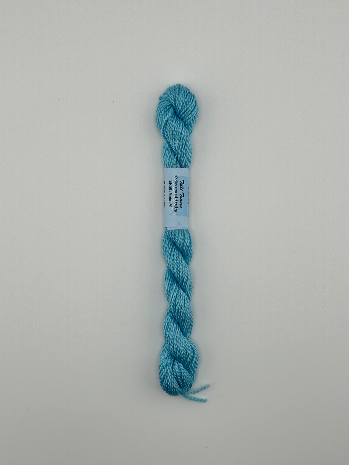 30 yard skein of essentials needlepoint thread in Sprinkler S696 blue, with blue label lying flat on white background