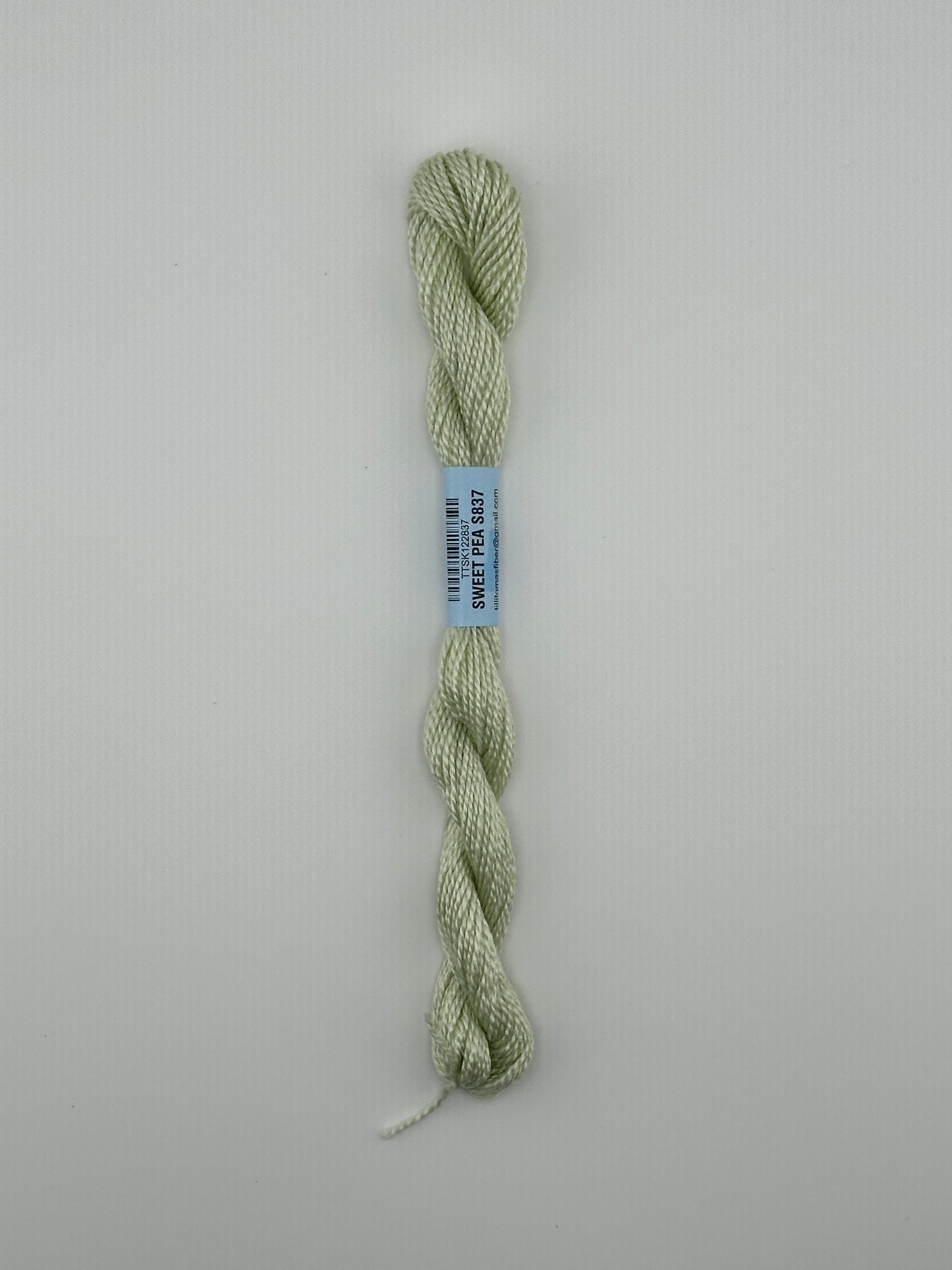 30 yard skein of essentials needlepoint thread in Sweet pea S837 green, with blue label lying flat on white background