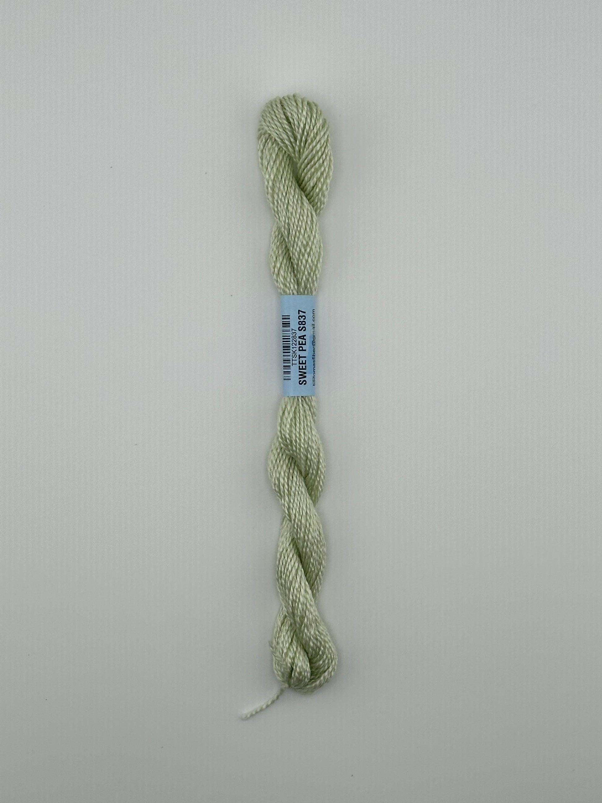 30 yard skein of essentials needlepoint thread in Sweet pea S837 green, with blue label lying flat on white background