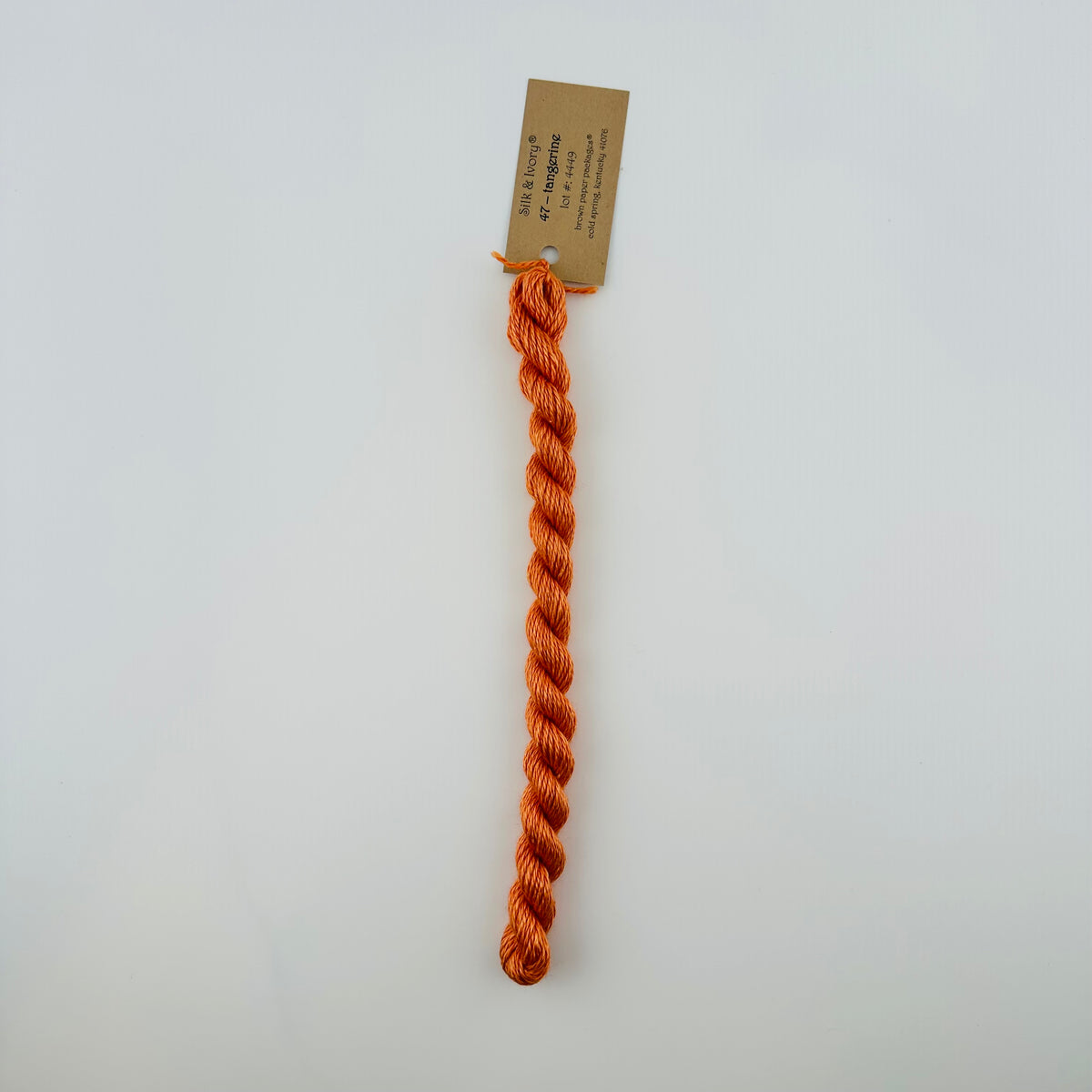 30 yard skein of silk & Ivory in the color 47 Tangerine with brown tag laying flat on white background