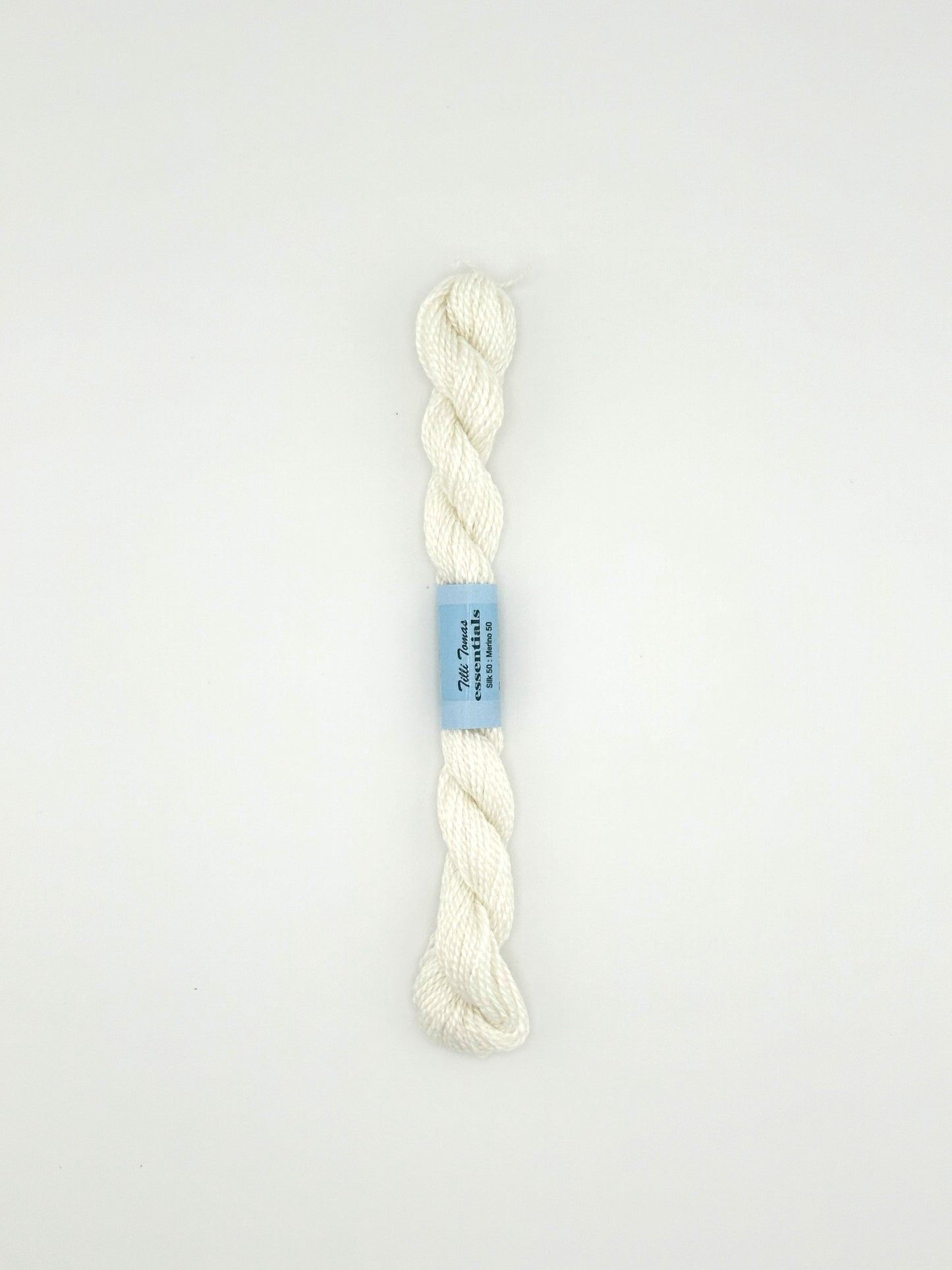 30 yard skein of essentials needlepoint thread in white 502, with blue label lying flat on white background