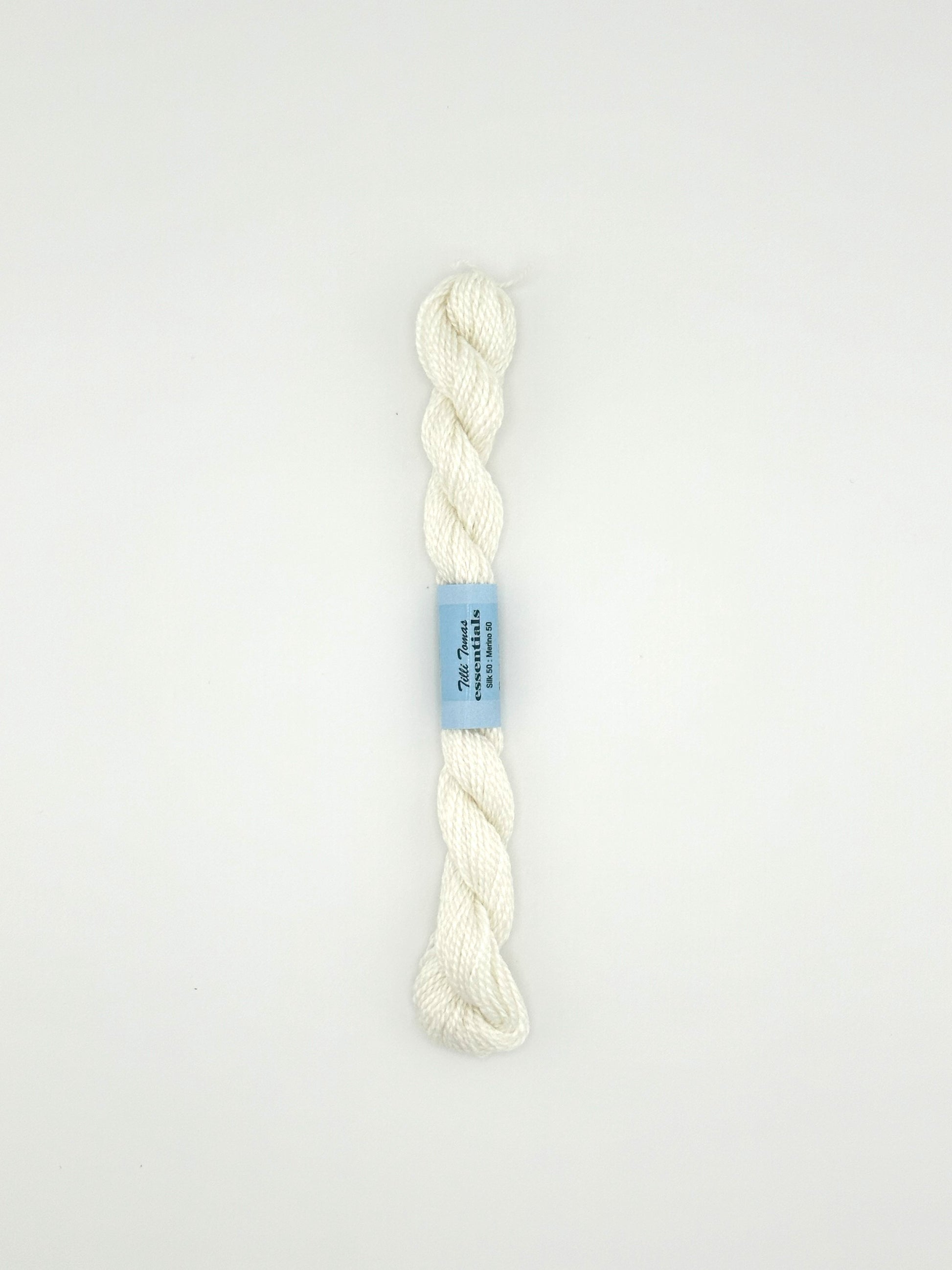 30 yard skein of essentials needlepoint thread in white 502, with blue label lying flat on white background