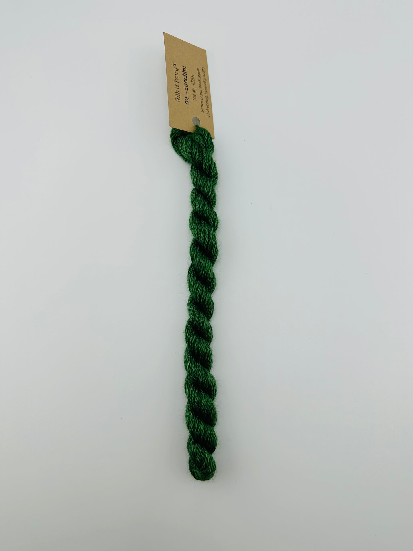 30 yard skein of silk & Ivory in the color 09 Zucchini with brown tag laying flat on white background