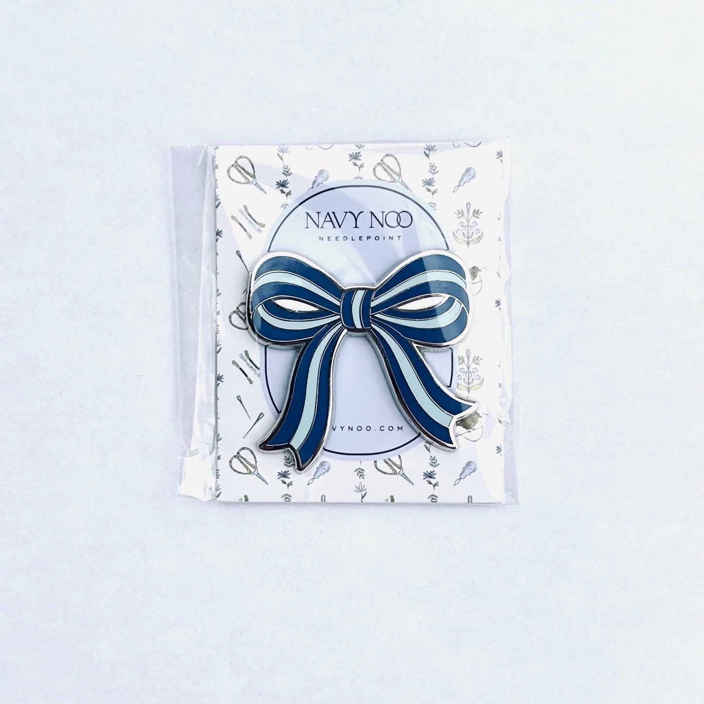A navy blue and white striped bow magnetic needle holder by Navy Noo, displayed on its branded white backing card inside a clear plastic sleeve, set against a clean white background.