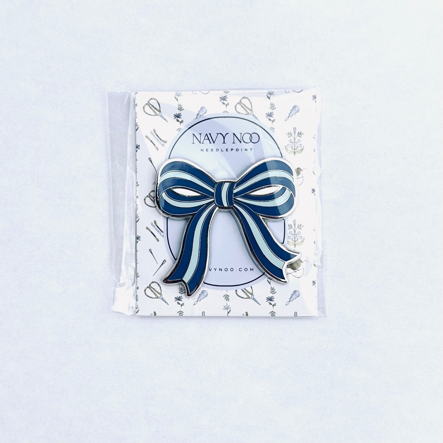 A navy blue and white striped bow magnetic needle holder by Navy Noo, displayed on its branded white backing card inside a clear plastic sleeve, set against a clean white background.