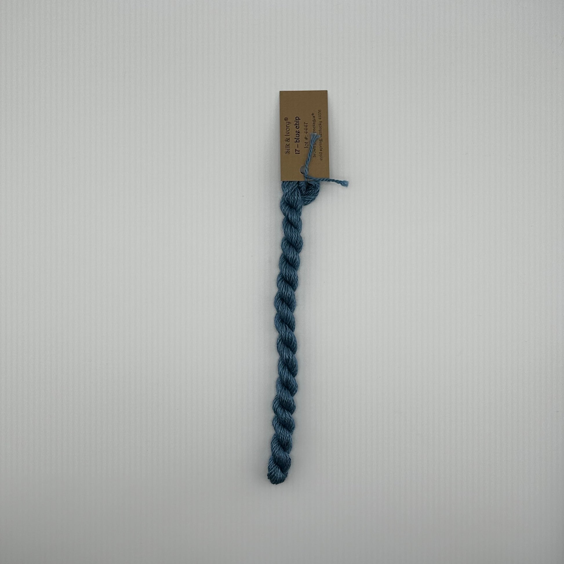 30 yard skein of silk & Ivory in the color 17 Blue Chip with brown tag laying flat on white background