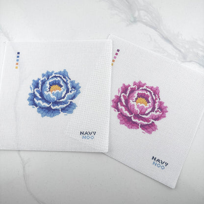two 18 mesh needlepoint canvas's featuring one blue and one pink peony flower with a yellow center, plus small color key squares on the left and the text 'NAVY NOO' on the bottom right, photographed on a white background.