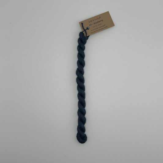 30 yard skein of silk & Ivory in the color 110 Blueberry with brown tag laying flat on white background