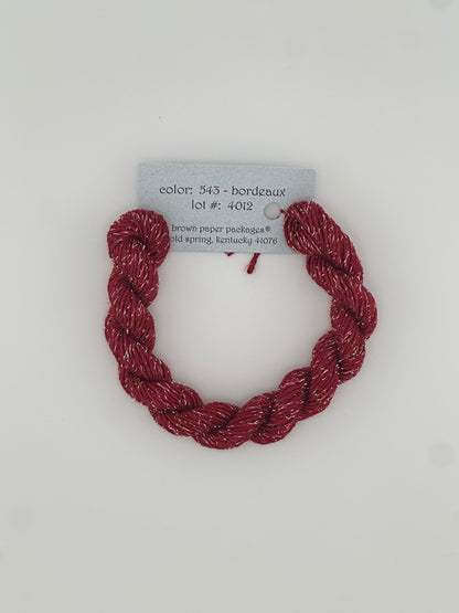 30 yard skein of Stardust Silk and Ivory needlepoint thread in Bordeaux 543, with light blue label lying flat on white background