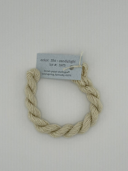 30 yard skein of Stardust Silk and Ivory needlepoint thread in Candlelight 534, with light blue label lying flat on white background