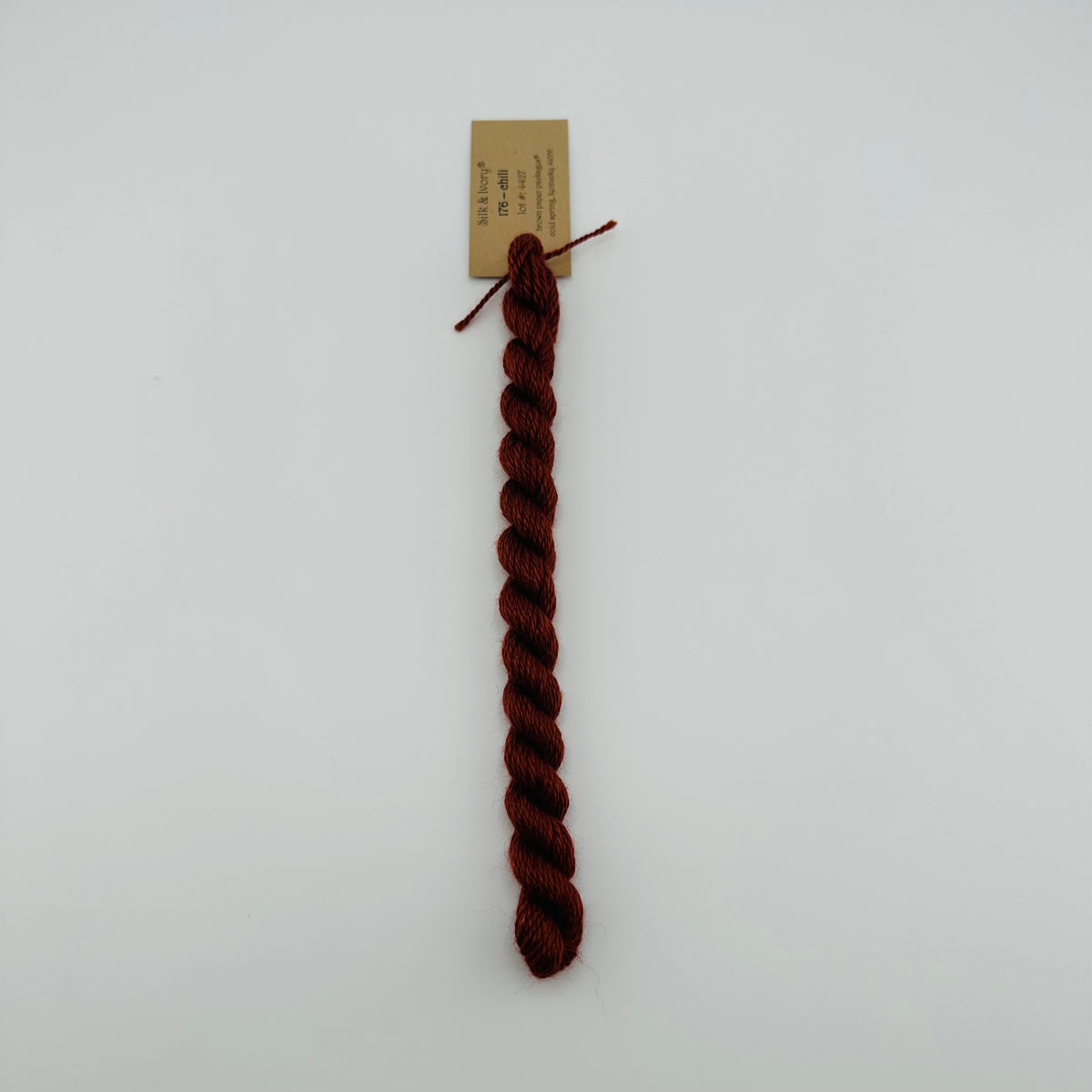 30 yard skein of silk & Ivory in the color 176 Chili with brown tag laying flat on white background