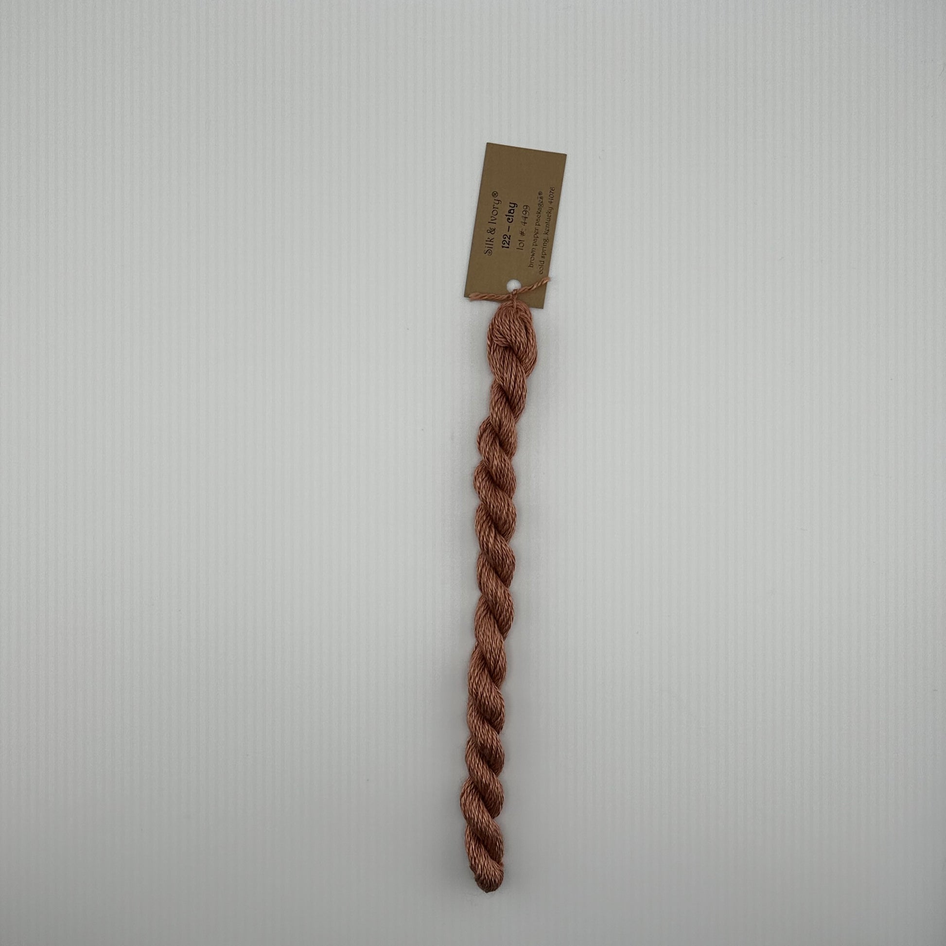 30 yard skein of silk & Ivory in the color 122 Clay with brown tag laying flat on white background