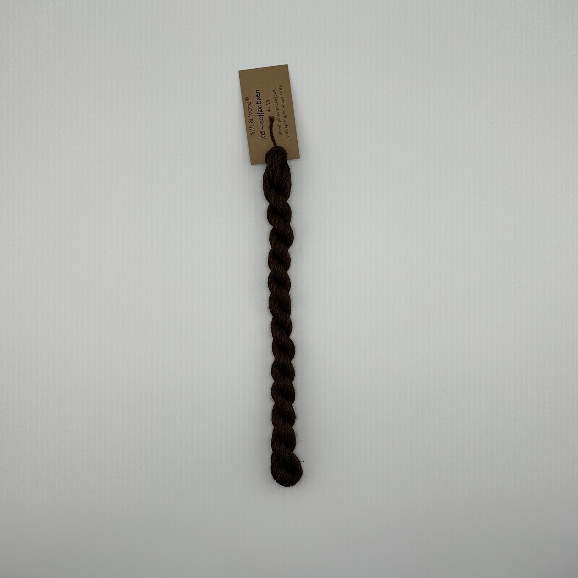 30 yard skein of silk & Ivory in the color 105 Coffee Bean with brown tag laying flat on white background