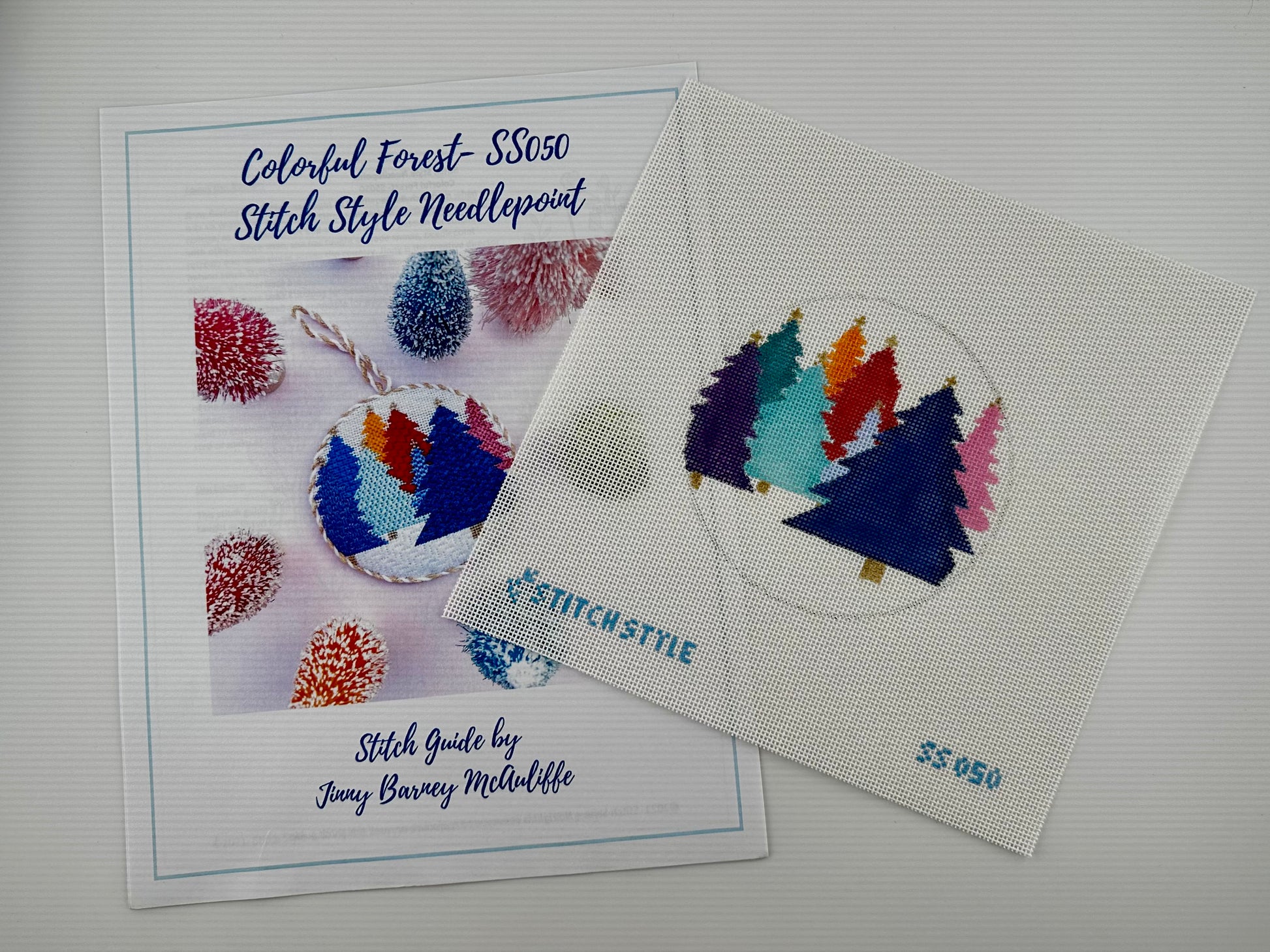 18 mesh needlepoint canvas featuring a circular design of colorful Christmas trees in purple, teal, light blue, red, orange, and pink on a white mesh background. The brand name 'STITCHSTYLE' is stitched in blue at the bottom left, and the number '35050' is stitched at the bottom right. shown with stitch guide.