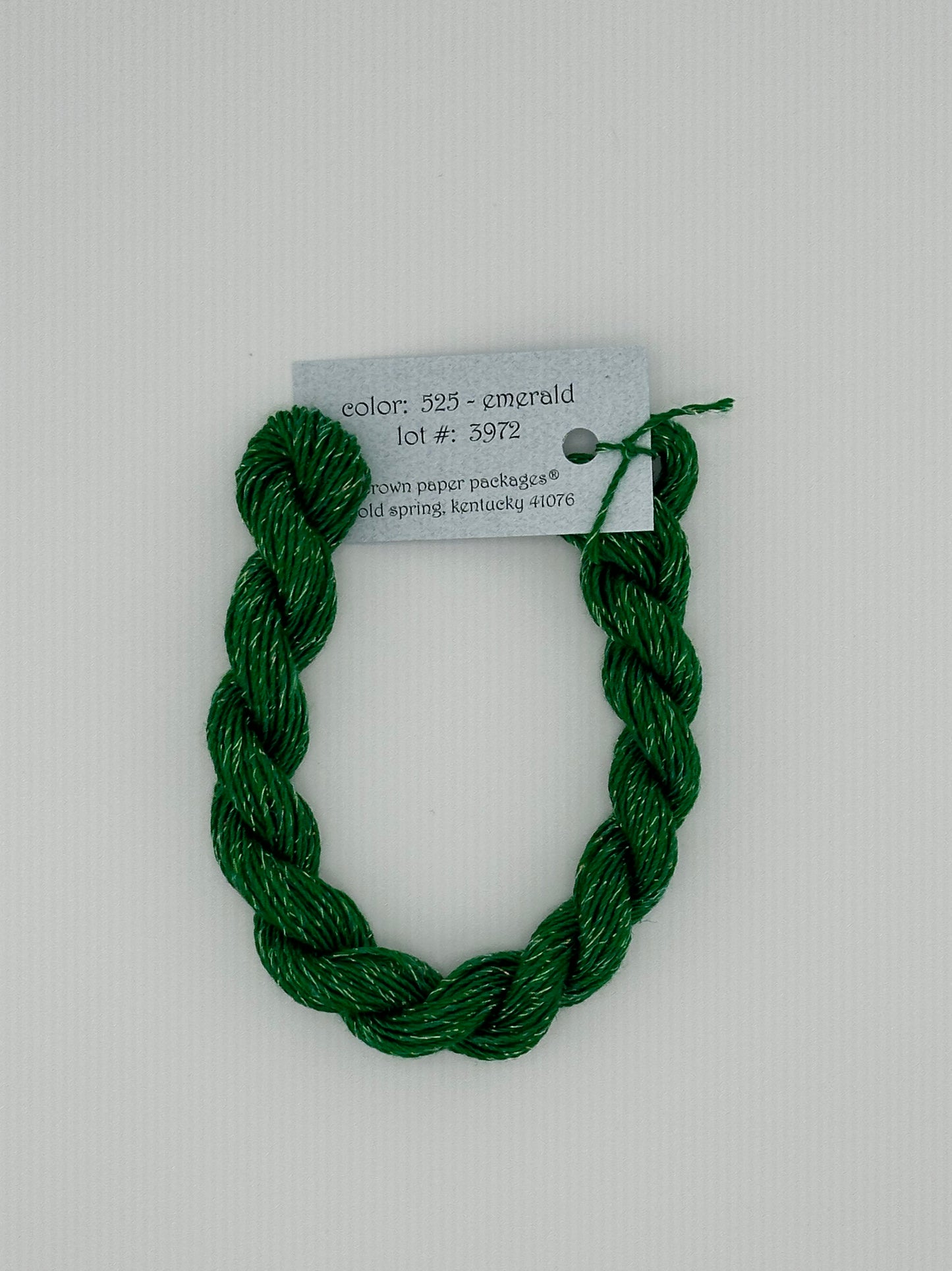 30 yard skein of Stardust Silk and Ivory needlepoint thread in Emerald 525, with light blue label lying flat on white background