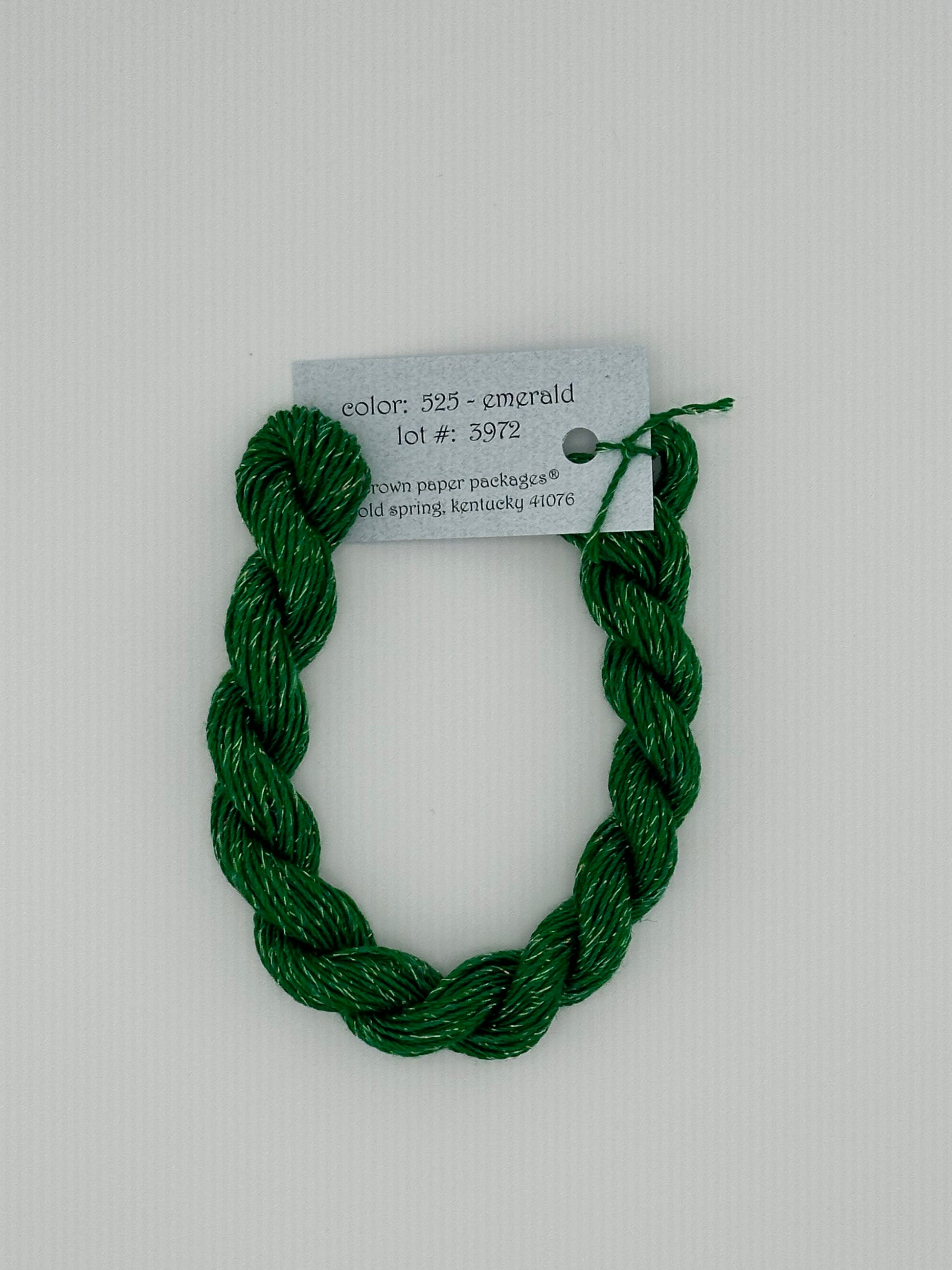 30 yard skein of Stardust Silk and Ivory needlepoint thread in Emerald 525, with light blue label lying flat on white background