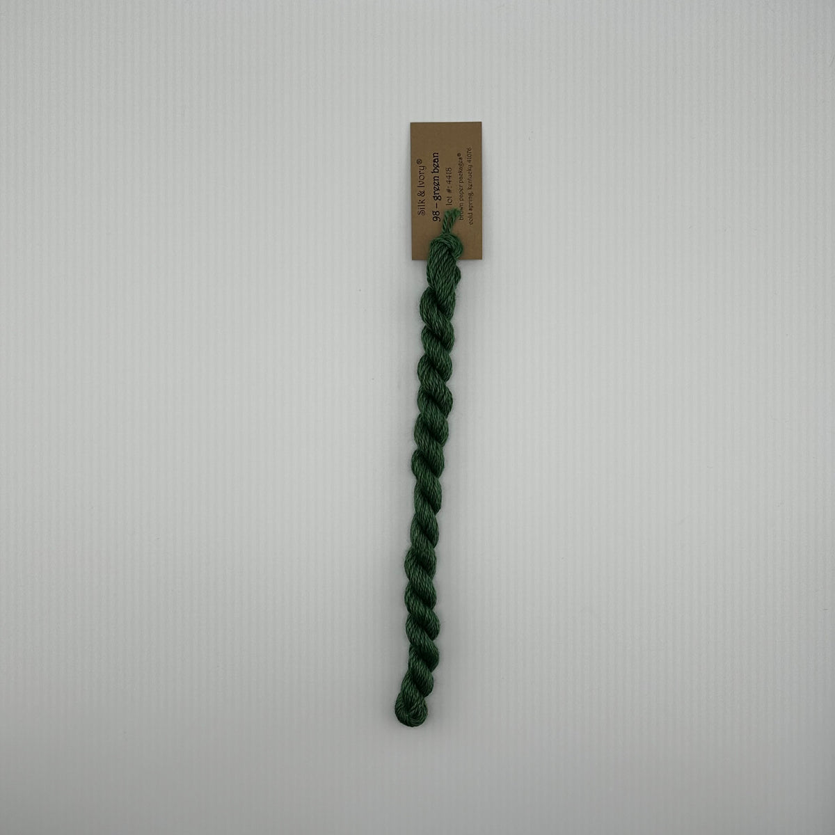 30 yard skein of silk & Ivory in the color 98 Green Bean with brown tag laying flat on white background