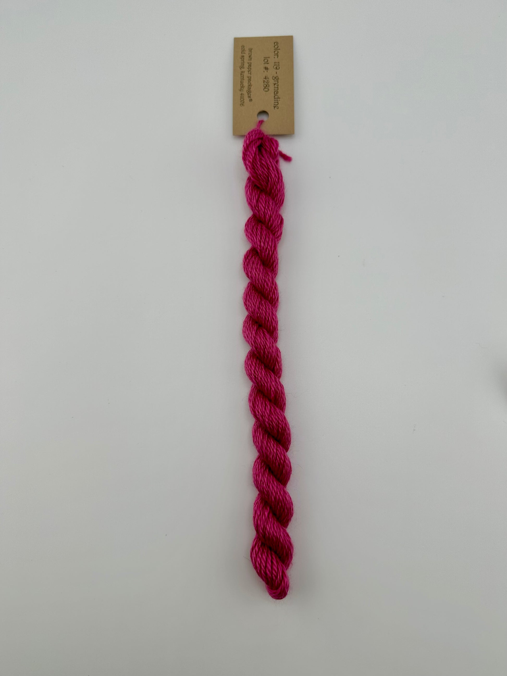 30 yard skein of silk & Ivory in the color 119 Grenadine with brown tag laying flat on white background