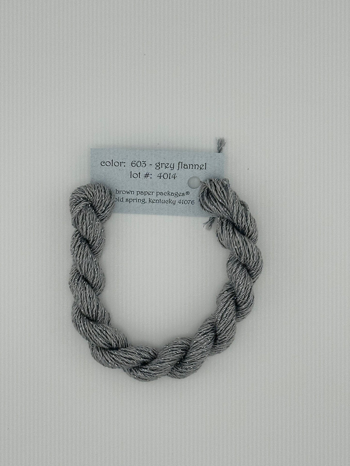 30 yard skein of Stardust Silk and Ivory needlepoint thread in Grey Flannel 603, with light blue label lying flat on white background