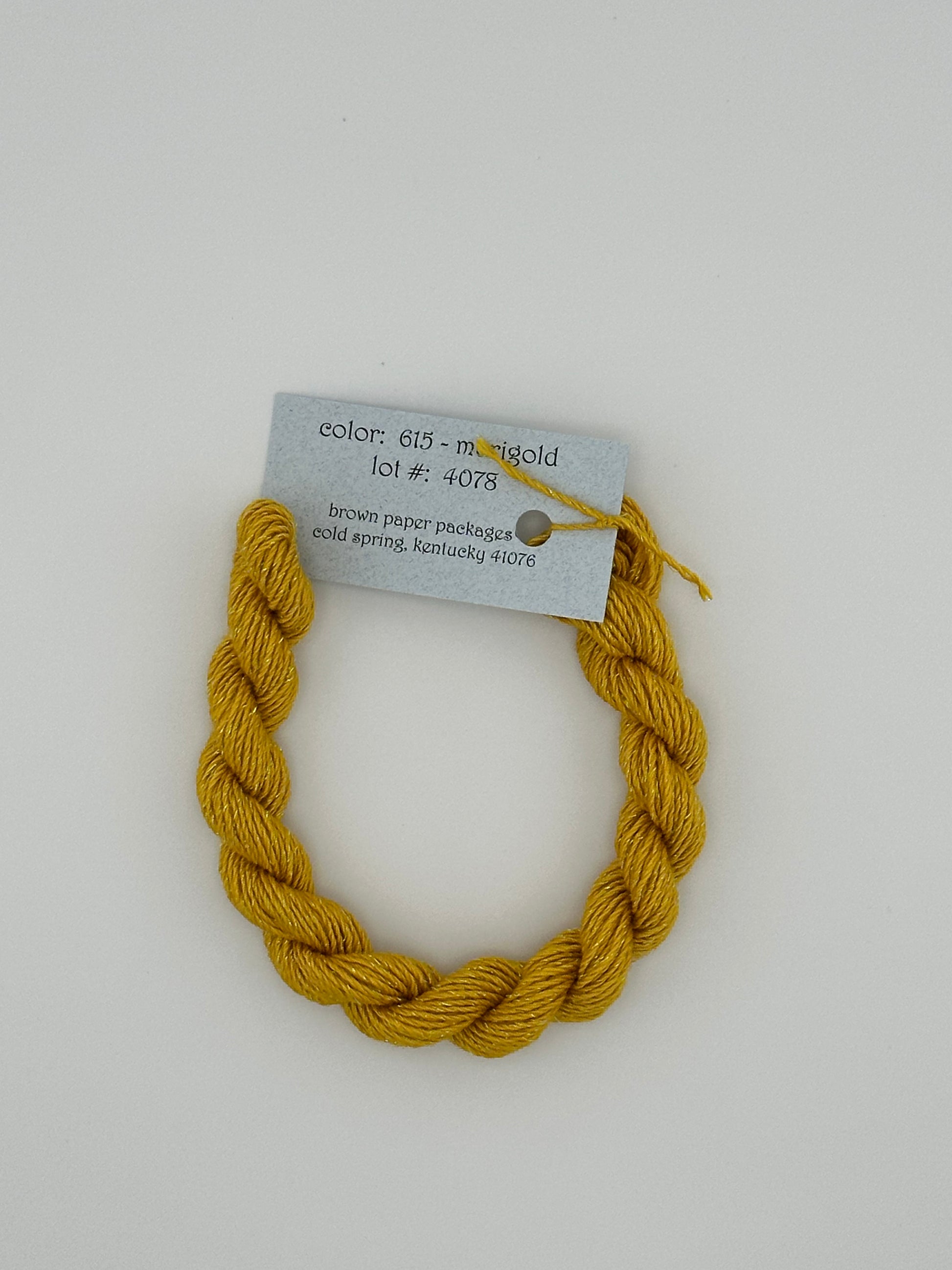 30 yard skein of Stardust Silk and Ivory needlepoint thread in Marigold 615, with light blue label lying flat on white background