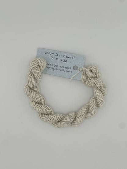 30 yard skein of Stardust Silk and Ivory needlepoint thread in Natural 501, with light blue label lying flat on white background