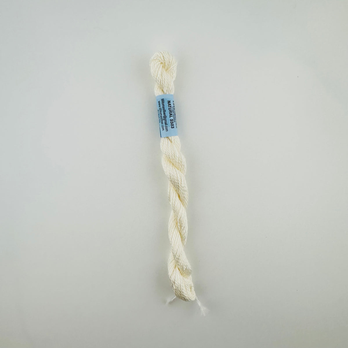 30 yard skein of essentials needlepoint thread in Natural S503, with blue label lying flat on white background