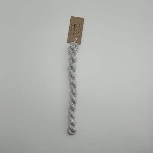 30 yard skein of silk & Ivory in the color 113 Pail Gray with brown tag laying flat on white background