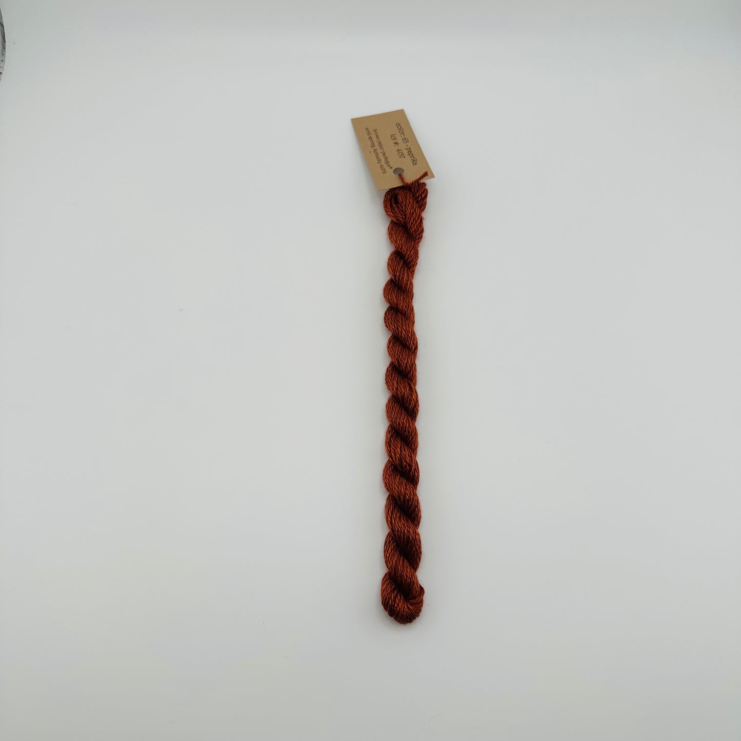 30 yard skein of silk & Ivory in the color 63 Paprika with brown tag laying flat on white background