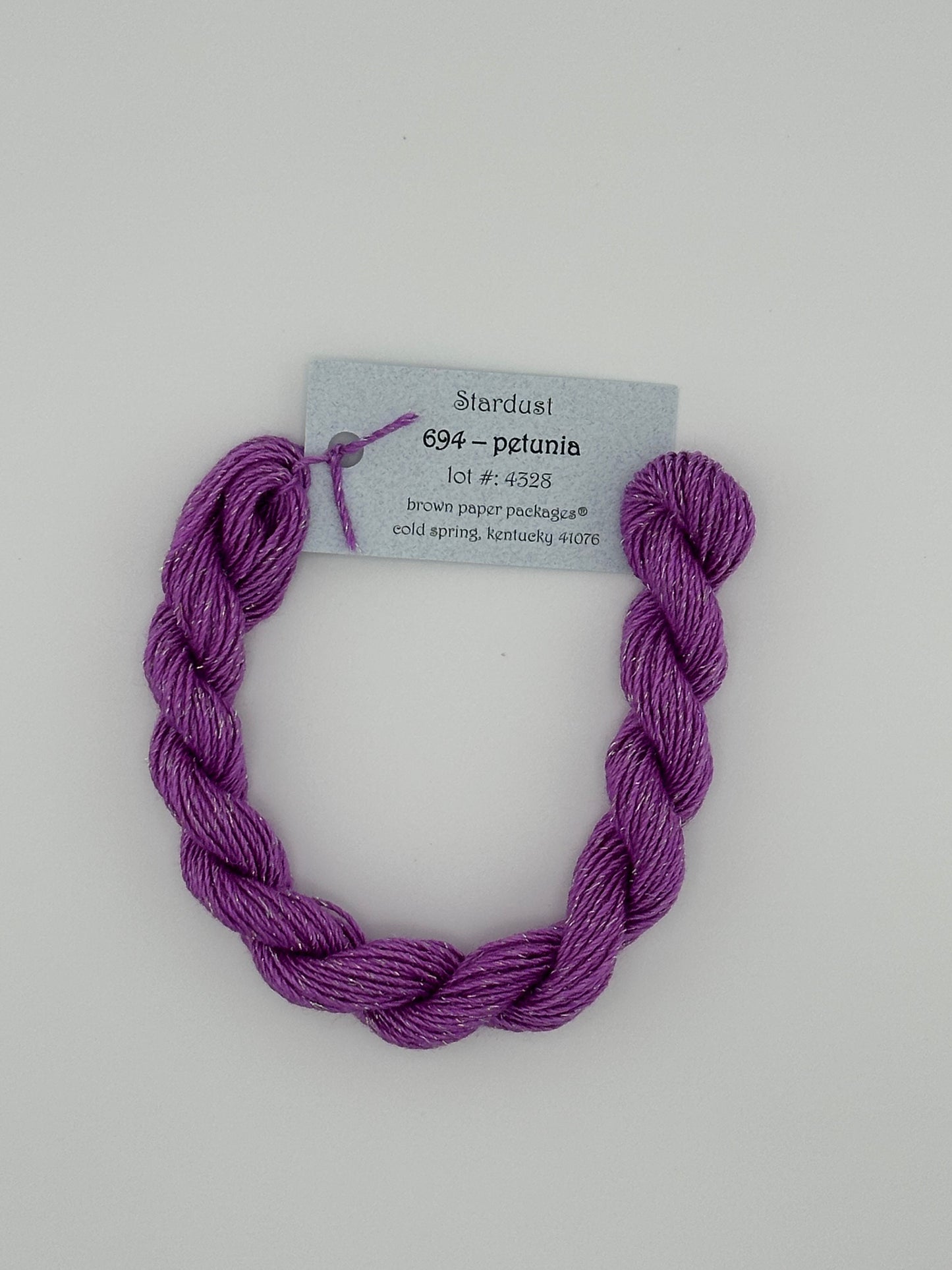 30 yard skein of Stardust Silk and Ivory needlepoint thread in Petunia 694, with light blue label lying flat on white background