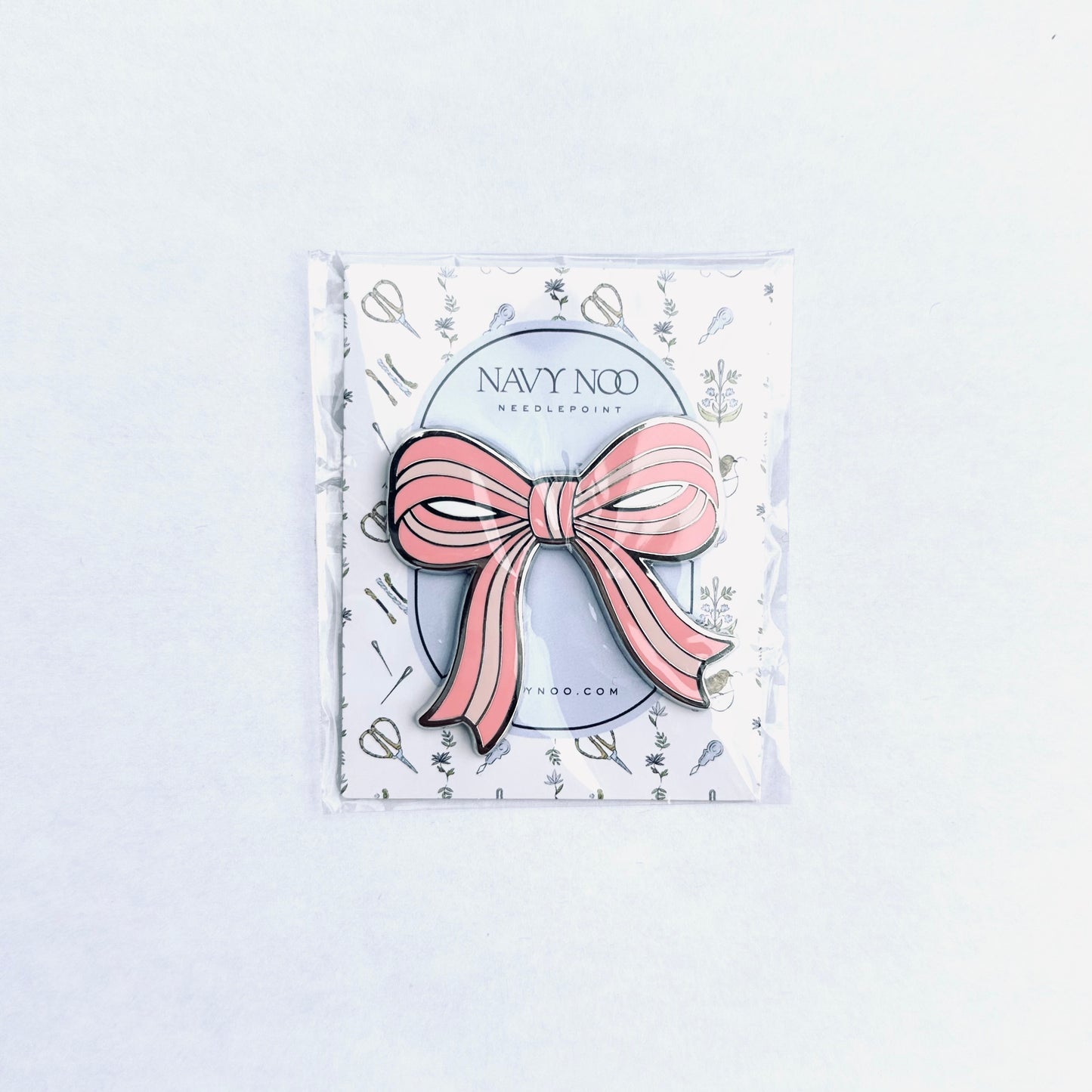 A pink and white striped bow magnetic needle holder by Navy Noo, displayed on its branded white backing card inside a clear plastic sleeve, set against a clean white background.