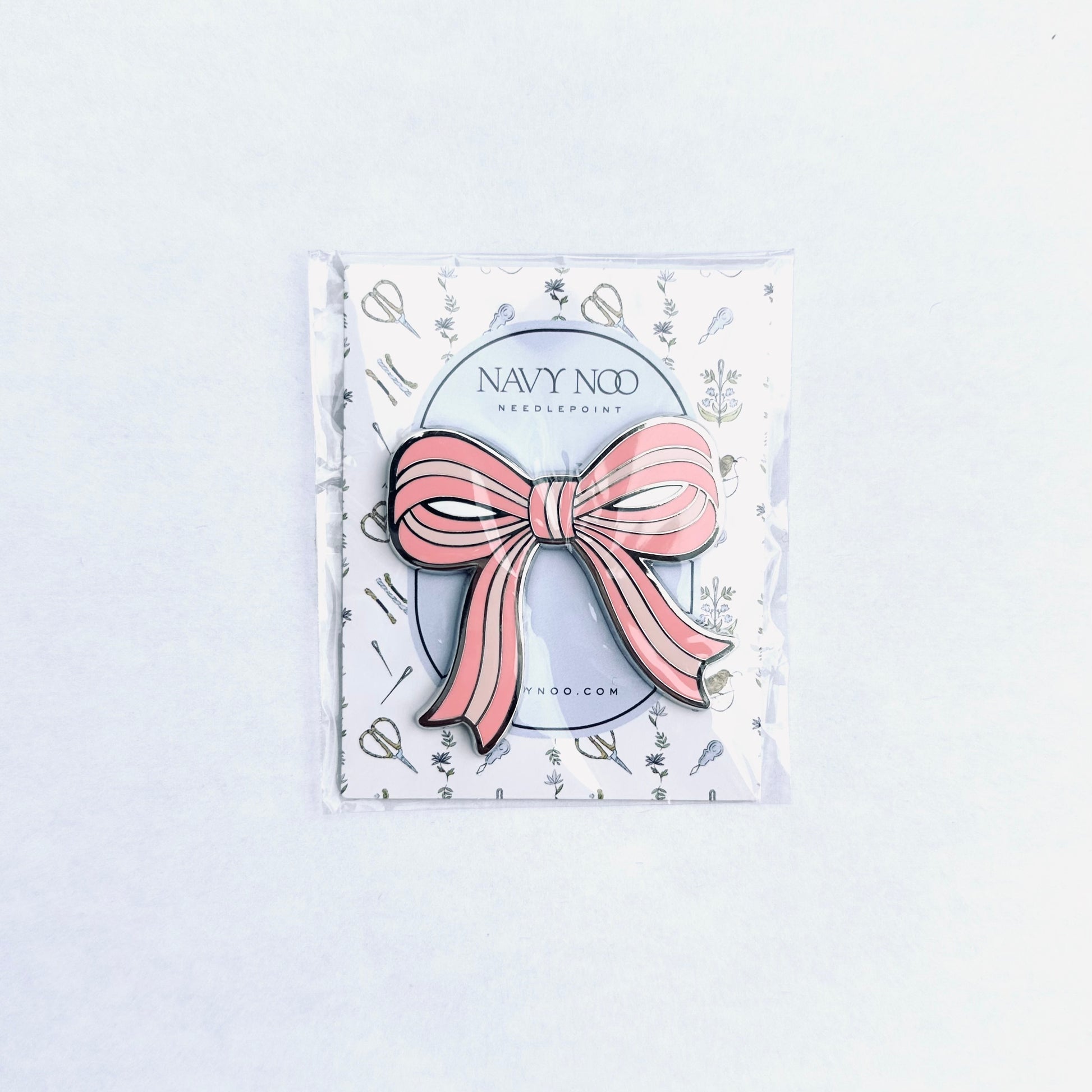 A pink and white striped bow magnetic needle holder by Navy Noo, displayed on its branded white backing card inside a clear plastic sleeve, set against a clean white background.