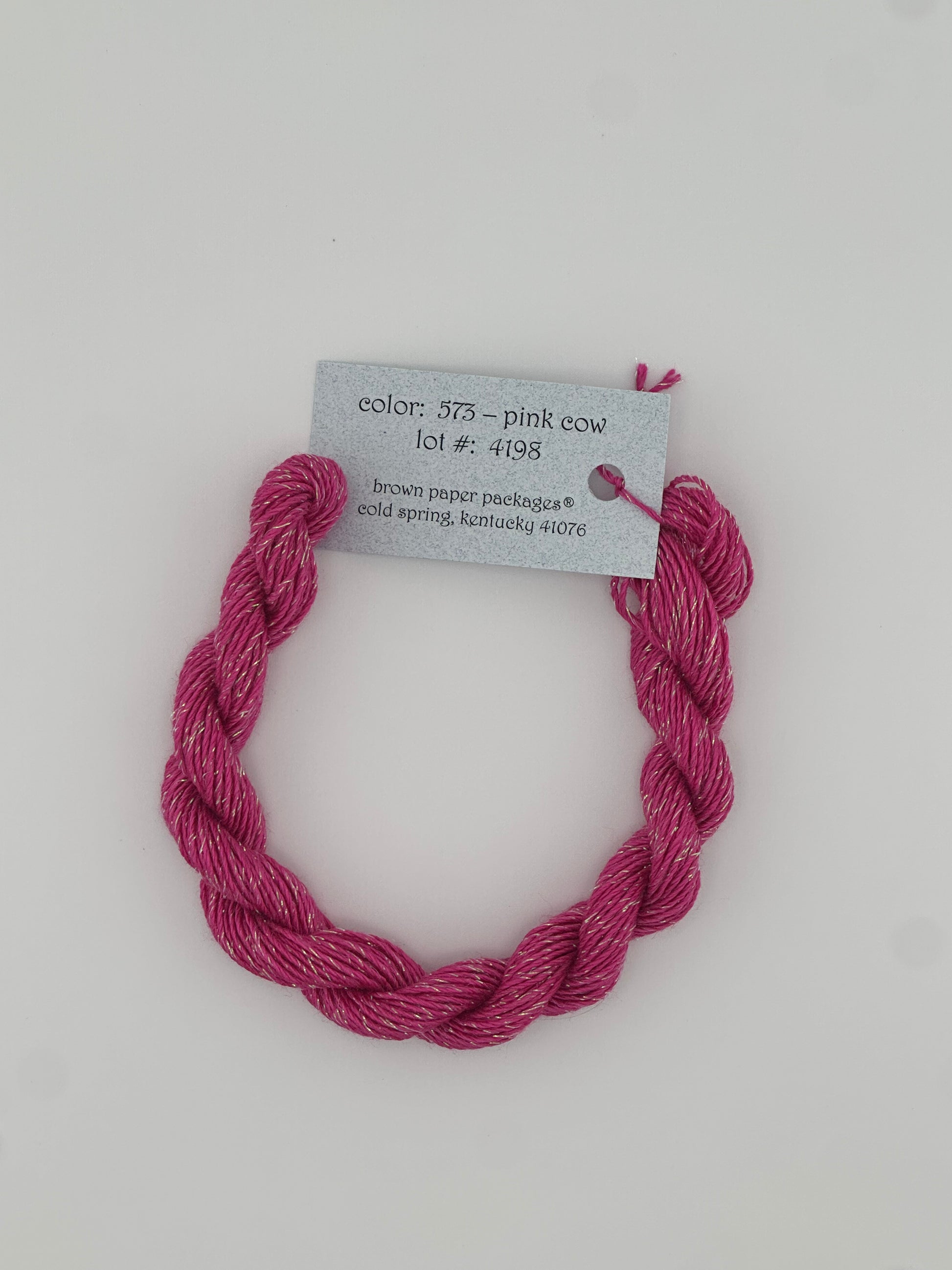 30 yard skein of Stardust Silk and Ivory needlepoint thread in Pink Cow 573, with light blue label lying flat on white background