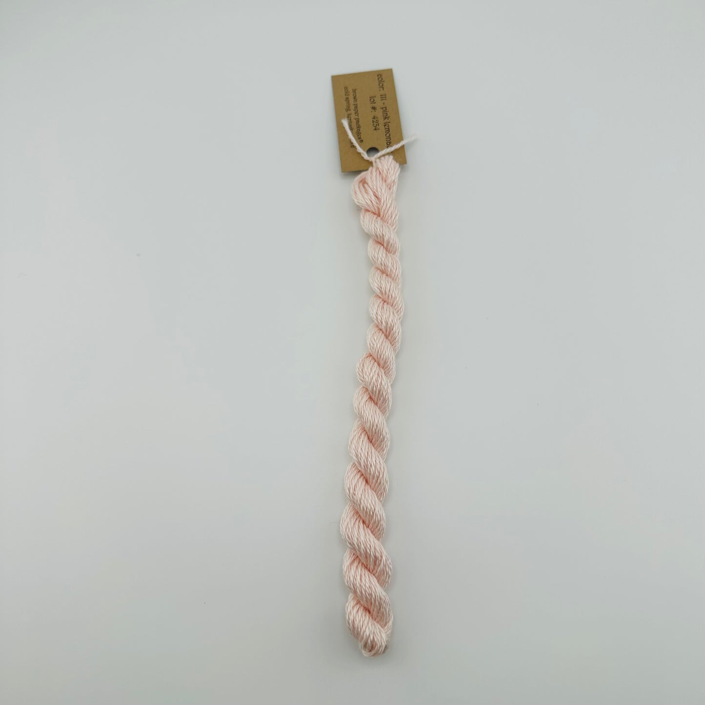 30 yard skein of silk & Ivory in the color 111 Pink Lemonade with brown tag laying flat on white background