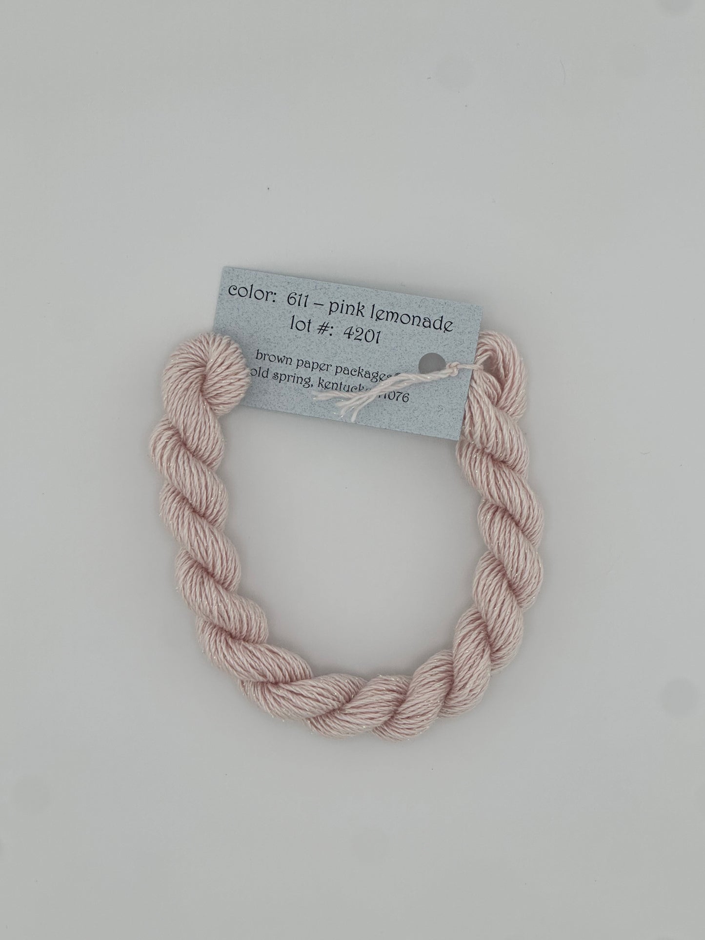 30 yard skein of Stardust Silk and Ivory needlepoint thread in Pink Lemonade 611, with light blue label lying flat on white background