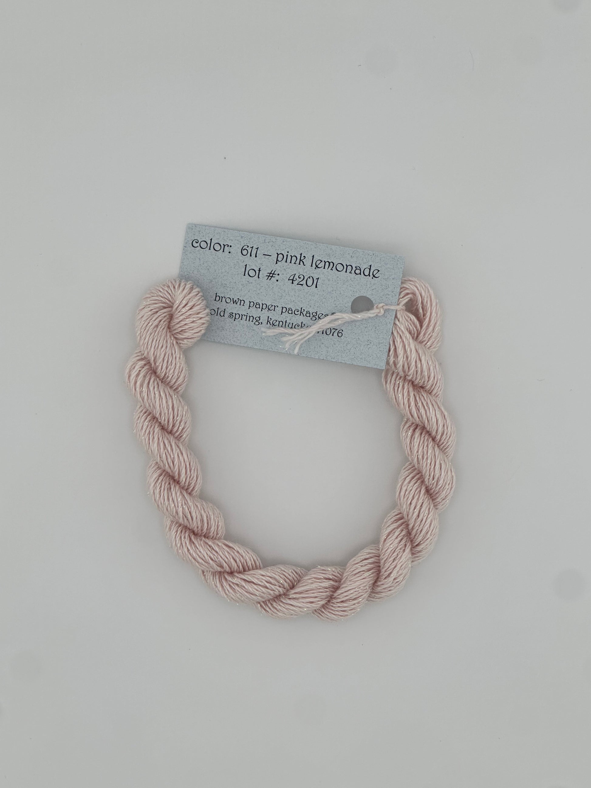 30 yard skein of Stardust Silk and Ivory needlepoint thread in Pink Lemonade 611, with light blue label lying flat on white background