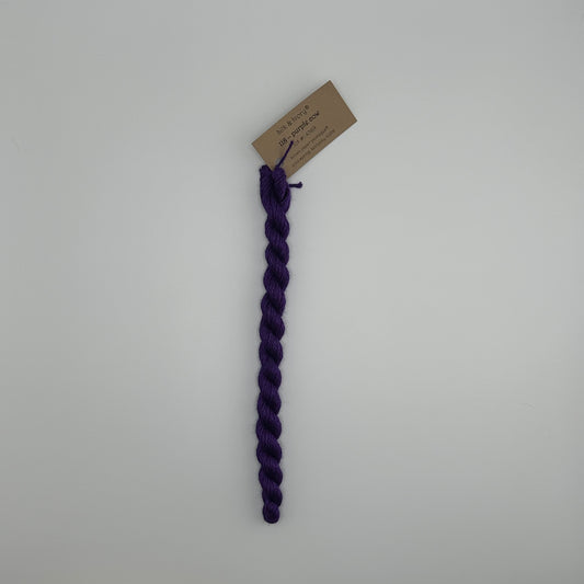 30 yard skein of silk & Ivory in the color 118 Purple Cow with brown tag laying flat on white background