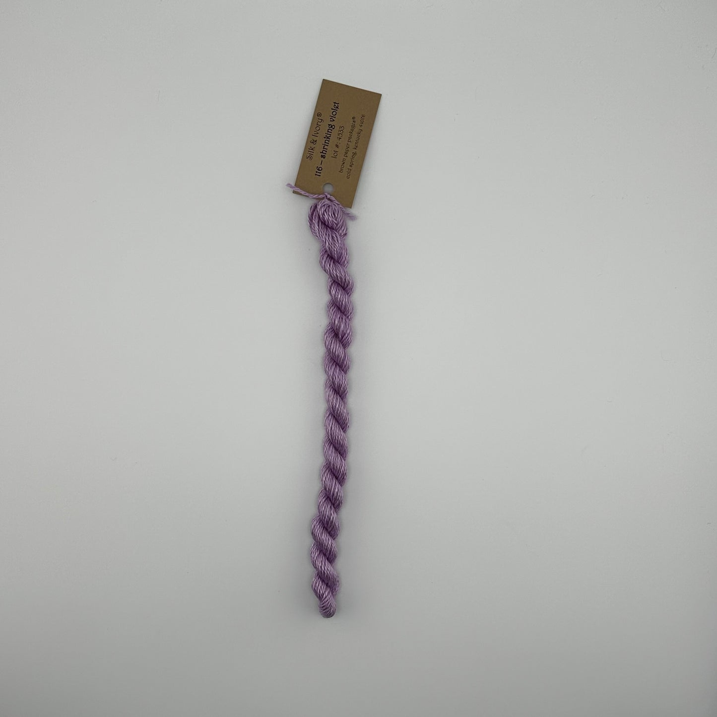 30 yard skein of silk & Ivory in the color 116 Shrinking Violet with brown tag laying flat on white background